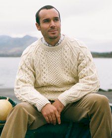 Man seated on sea wall wearing cream coloured Aran knitwear