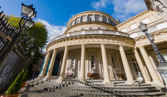 Wideangle view of National Library of Ireland in Dublin, focussing on stone steps and columns of entrance, dome of the Reading Room and wrought iron railings and street lamps.