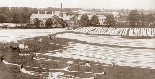Vintage photo showing strips of linen being laid out in the fields (known as Bleaching Greens) surrounding an old mill in Co Antrim