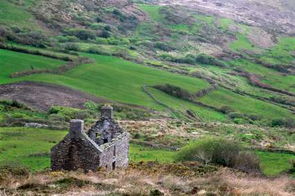 Hilly landscape in Ireland with patchwork fields and a house ruin in the near-view.