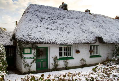 A traditional thatched cottage, whitewashed and with glossy mid-green painted woodwork, in Adare, Co Limerick, Ireland.