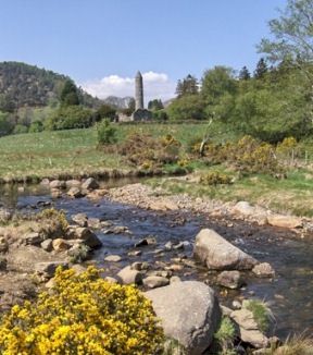 Distant view, across rocky stream and fields, to the medieval Round Tower at Glendalough, Co Wicklow.