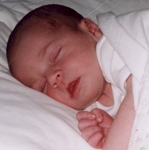 One-day-old infant, asleep, resting on pillow.