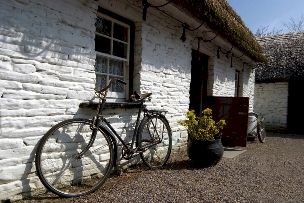 Whitewashed thatched cottage with vintage bike propped against wall.