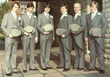 A father with his five young adult sons, all dressed in grey 'top hat and tails' wedding outfits, pose outside church.